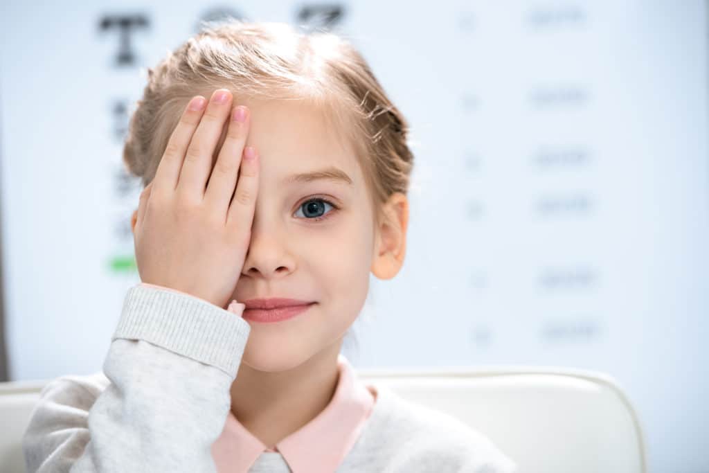 little girls covering one eye with her hand with blurred mostly white background