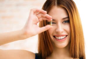 smiling woman covering her eye looking through Omega 3 fish oil capsule.