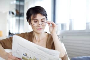 Woman wears reading glasses so she can see her newspaper at the kitchen table